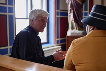Senior priest discussing christian moments with woman while they sitting on bench in church