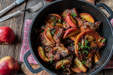 Braised pork cutlets with apples and onions in a roasting pot on wooden table