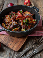Pork chops with braised with apples and onions in a pot on wooden table 