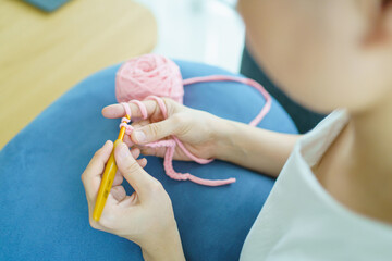 Happy cheerful Asian woman doing a crochet in living room in free time. Skillful Asian craftswoman knitting a handcraft crochet sweater and hat in cozy living room.
