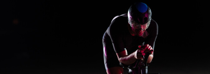 A triathlete rides his bike in the darkness of night, pushing himself to prepare for a marathon. The contrast between the darkness and the light of his bike creates a sense of drama and highlights the