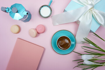 A cup of coffee and a gift box with a white bow on a pink background.