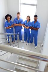 Portrait Of Multi Cultural Medical Team Wearing Scrubs Standing On Stairs In Hospital 