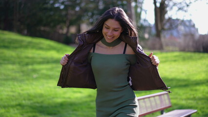 One carefree young woman feeling joy while dancing at park celebrating success. Happiness concept of an adult girl in 20s jumping up and down feeling ecstatic