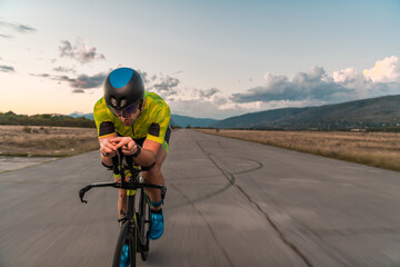  Triathlete riding his bicycle during sunset, preparing for a marathon. The warm colors of the sky provide a beautiful backdrop for his determined and focused effort.