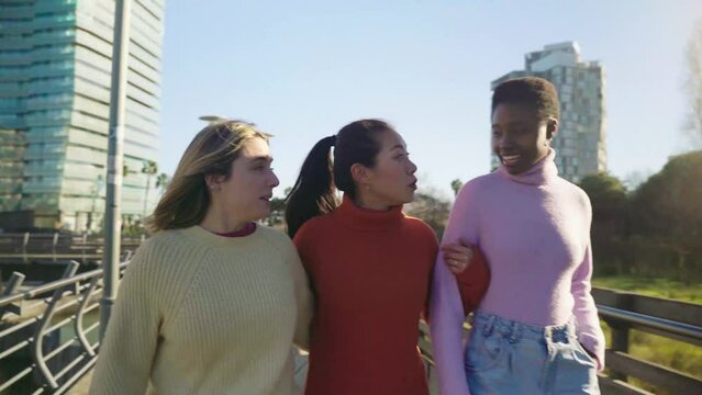 Three female friends walking and talking arm in arm outdoors in the city during a sunny day. Having a good time together. High quality 4k footage