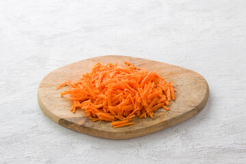 Wooden board with grated carrots on a light gray background, top view