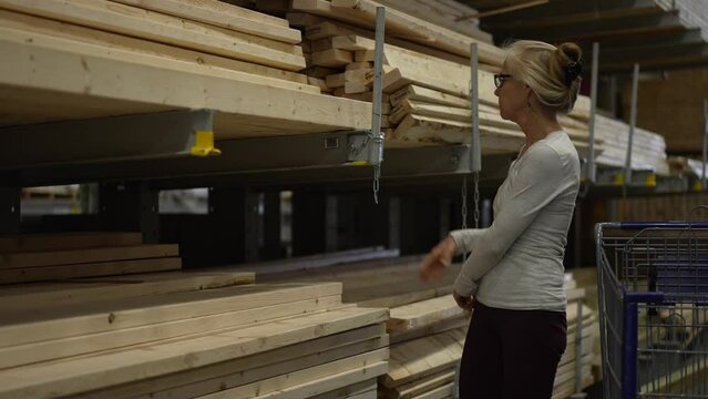 Mature woman picking wood two by fours for construction project in the lumber section of a big box hardware store.