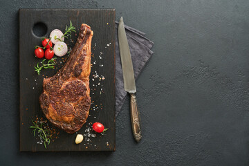 Tomahawk steak. Sliced grilled tomahawk beef steak with baked cherry tomatoes, herbs and salt on old wooden background. Preparing to grill.  Top view and copy space.