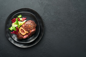 Steaks Osso Buco. Sliced beef grilled Osso Buco or porterhouse meat steak with garnished with salad and french fries on black marble board on old wooden background. Top view. Mock up.