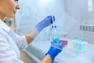 Unrecognizable scientist holding test tube with reagent, dropping color liquid over glass equipment.