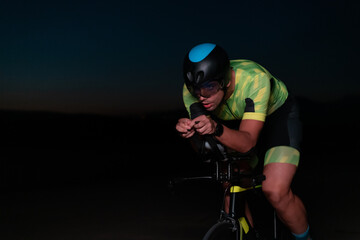 Obraz na płótnie Canvas A triathlete rides his bike in the darkness of night, pushing himself to prepare for a marathon. The contrast between the darkness and the light of his bike creates a sense of drama and highlights the