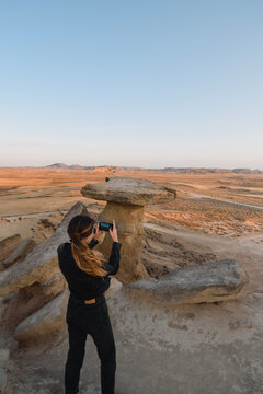 Girl photographer in the desert at sunset taking a photo with her smartphone
