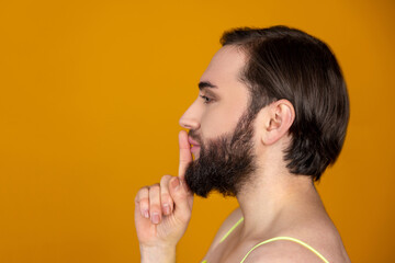 Side view of bearded transsexual person holding finger near lips making silence gesture keeps secret