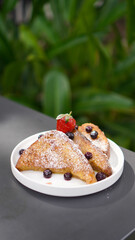 Delicious french toast with fresh fruits and maple sirup. Tasty breakfast scene or dessert with toast, strawberries, blueberries and powdered sugar.
