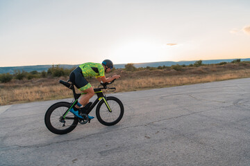  Triathlete riding his bicycle during sunset, preparing for a marathon. The warm colors of the sky provide a beautiful backdrop for his determined and focused effort.