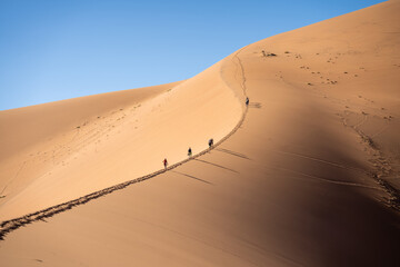 Fototapeta na wymiar people walking on red sand dunes in the desert with blue sky