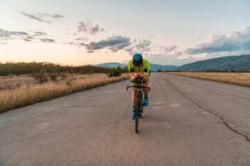  Triathlete riding his bicycle during sunset, preparing for a marathon. The warm colors of the sky provide a beautiful backdrop for his determined and focused effort.