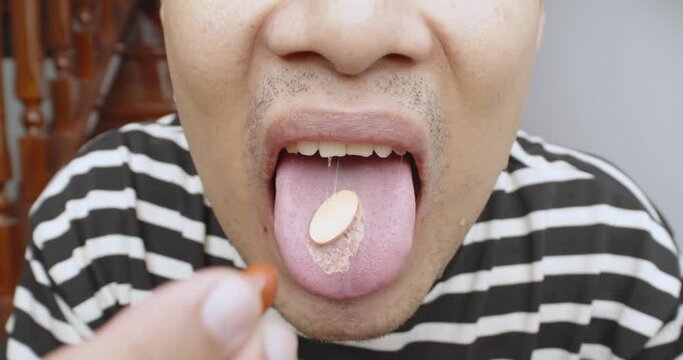 A man puts a pill on his tongue close up. Shot of man mouth with vitamin capsule. Micro dosing for depression treatment. Vitamins and supplements preventive medicine.