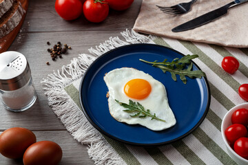 Fried eggs for breakfast. Healthy breakfast with vegetables and herbs. Fried egg on a blue plate. Serving on the table 