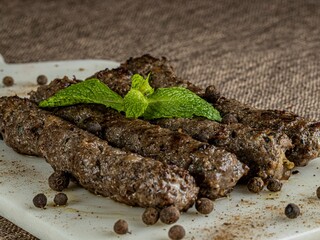 Square platter with pieces of grilled meat and a few sprigs of peppers, ready to be served