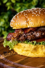 Freshly prepared hamburger on a wooden cutting board, with lettuce and bacon