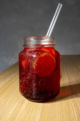 Canning jar filled with red tasty lemonade with a straw on a table top