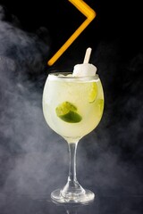 Glass of a cold beverage with lime, with smoke on the background