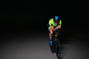 A triathlete rides his bike in the darkness of night, pushing himself to prepare for a marathon. The contrast between the darkness and the light of his bike creates a sense of drama and highlights the
