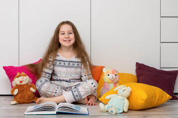 laughing girl with long hair sits surrounded by colorful pillows with toys and an open book