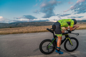 Fototapeta premium Triathlete riding his bicycle during sunset, preparing for a marathon. The warm colors of the sky provide a beautiful backdrop for his determined and focused effort.