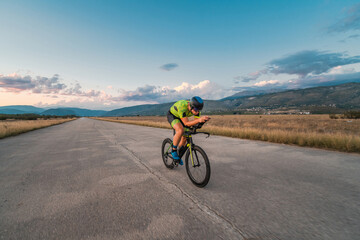  Triathlete riding his bicycle during sunset, preparing for a marathon. The warm colors of the sky...