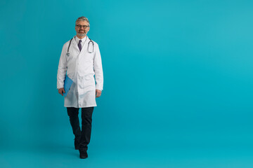 Cheerful middle aged doctor with medical chart walking on blue