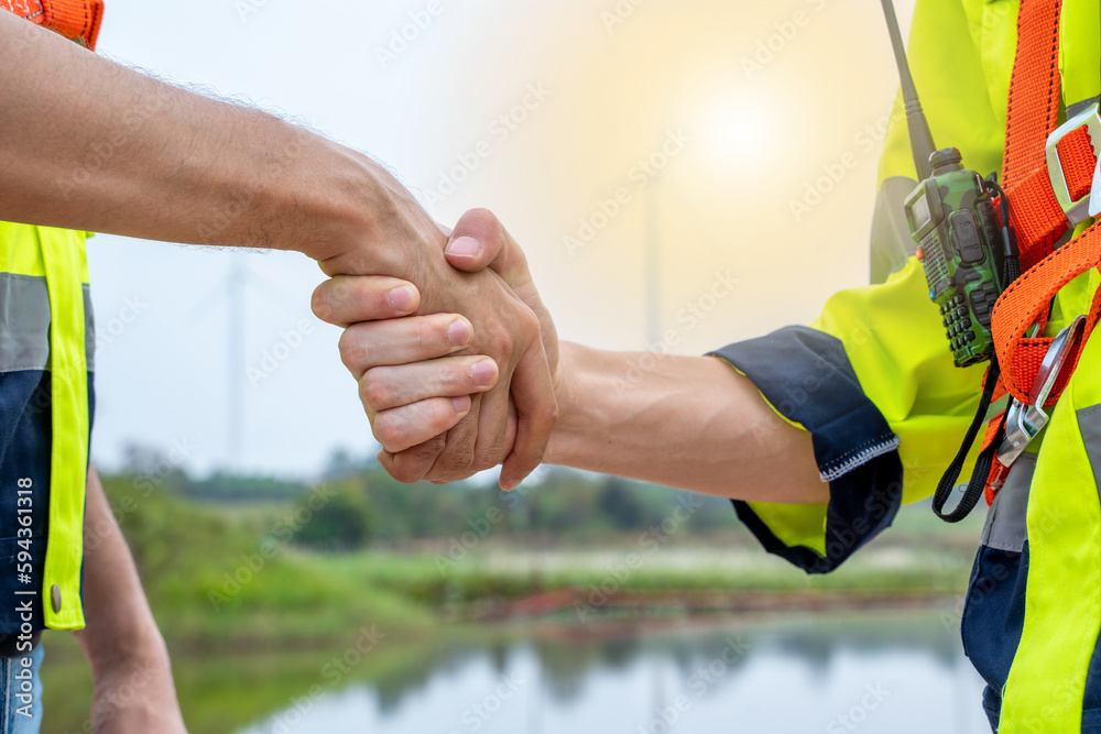 Poster engineers handshake after inspection work in wind turbine power generator station.
