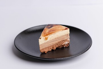 Slice of decadent brown cheesecake, topped with a layer of creamy white frosting and caramel sauce