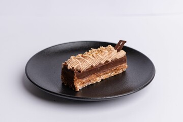 Black ceramic plate with a rich, chocolate cake topped with a layer of creamy, white frosting