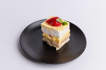 Delicious piece of white Shortcake on a black plate, decorated with fresh red strawberries