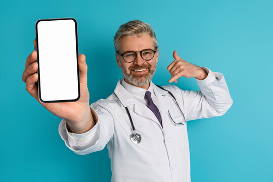 Cheerful middle aged doctor showing smartphone with white screen