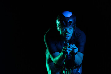 A triathlete rides his bike in the darkness of night, pushing himself to prepare for a marathon. The contrast between the darkness and the light of his bike creates a sense of drama and highlights the