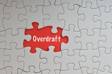 Fototapeta premium Missing jigsaw puzzle with text OVERDRAFT isolated on a red background.