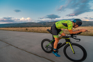  Triathlete riding his bicycle during sunset, preparing for a marathon. The warm colors of the sky...