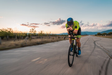  Triathlete riding his bicycle during sunset, preparing for a marathon. The warm colors of the sky...