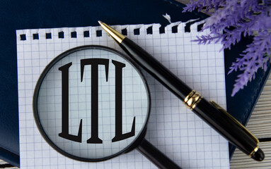 The letters LTL under a magnifying glass on a white piece of paper against the background of a fragment of a notebook and a pen