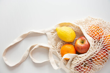 The string bag of natural material with fruits is on a white background. The theme of eco-friendly consumption. Copy space.
