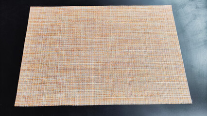 Brown or beige woven napkin, similar to burlap on a black surface. Background, texture, frame and copy space. The concept of beautiful decor and comfort in the house