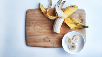 Banana with open panel on wooden board and sliced round pieces on the plate on white background. Ripe banana with peel and cooking, Close up. Delicious sweet fruit dessert