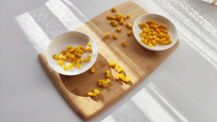 Lot of pieces of canned yellow corn on plate which is on wooden bamboo cutting board on white background. The concept of cooking and delicious healthy food