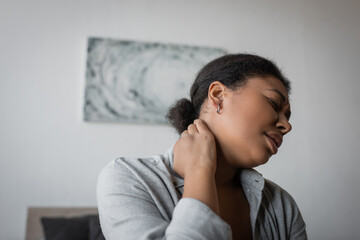 Young multiracial woman touching painful neck at home.