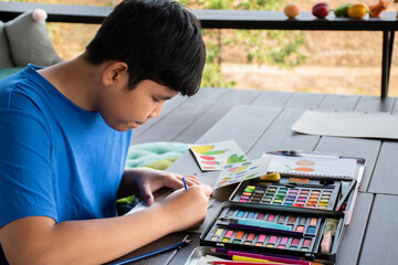Asian boy spending his free times with drawing, sketching, coloring by using watercolor in the...