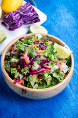 Fresh vegetable salad with purple cabbage, white cabbage, lettuce, and carrot, in a wooden bowl on a blue wooden background.